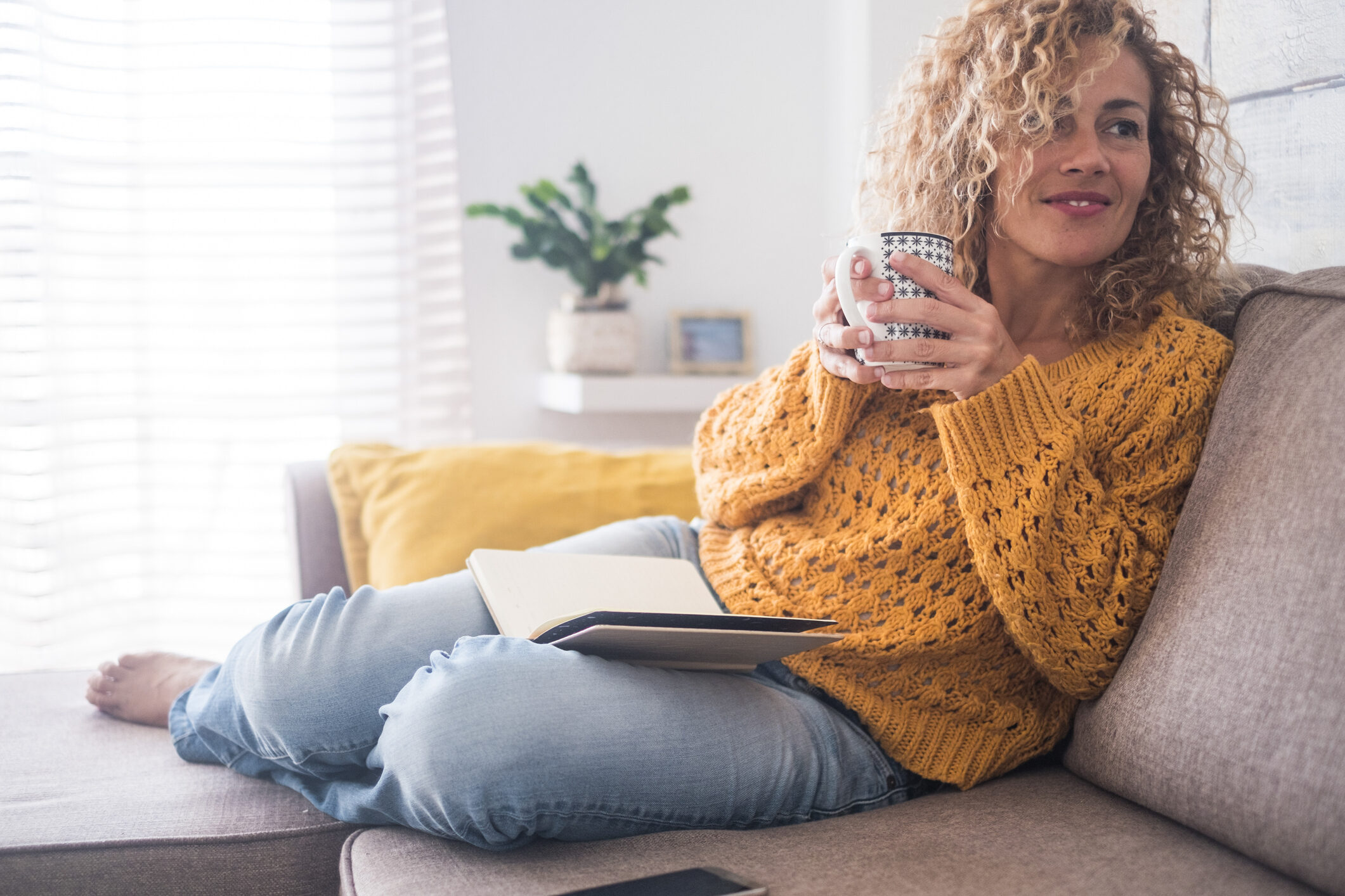 woman on couch with coffee, yellow sweater
