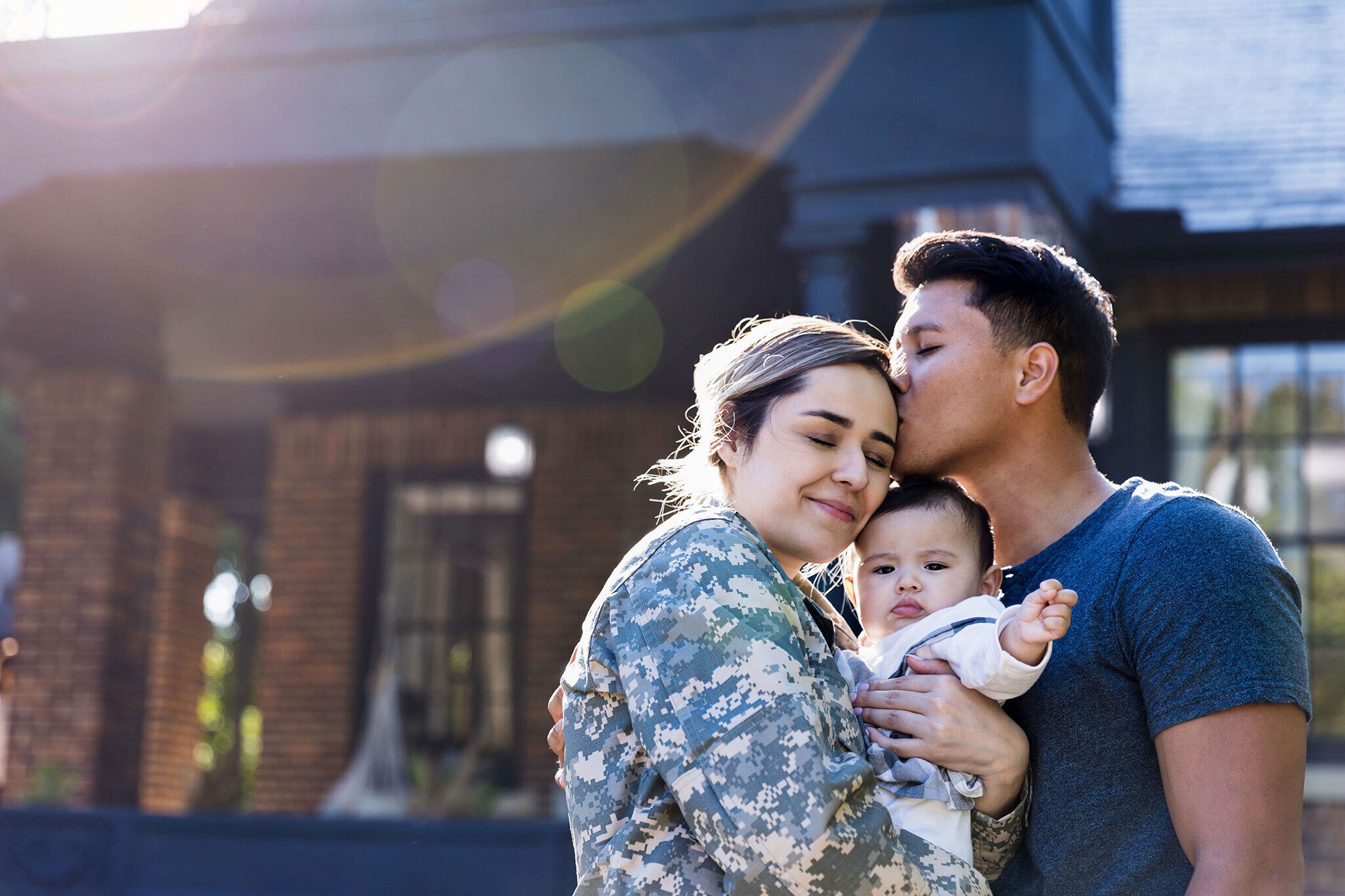 Military family standing in front of home with their baby