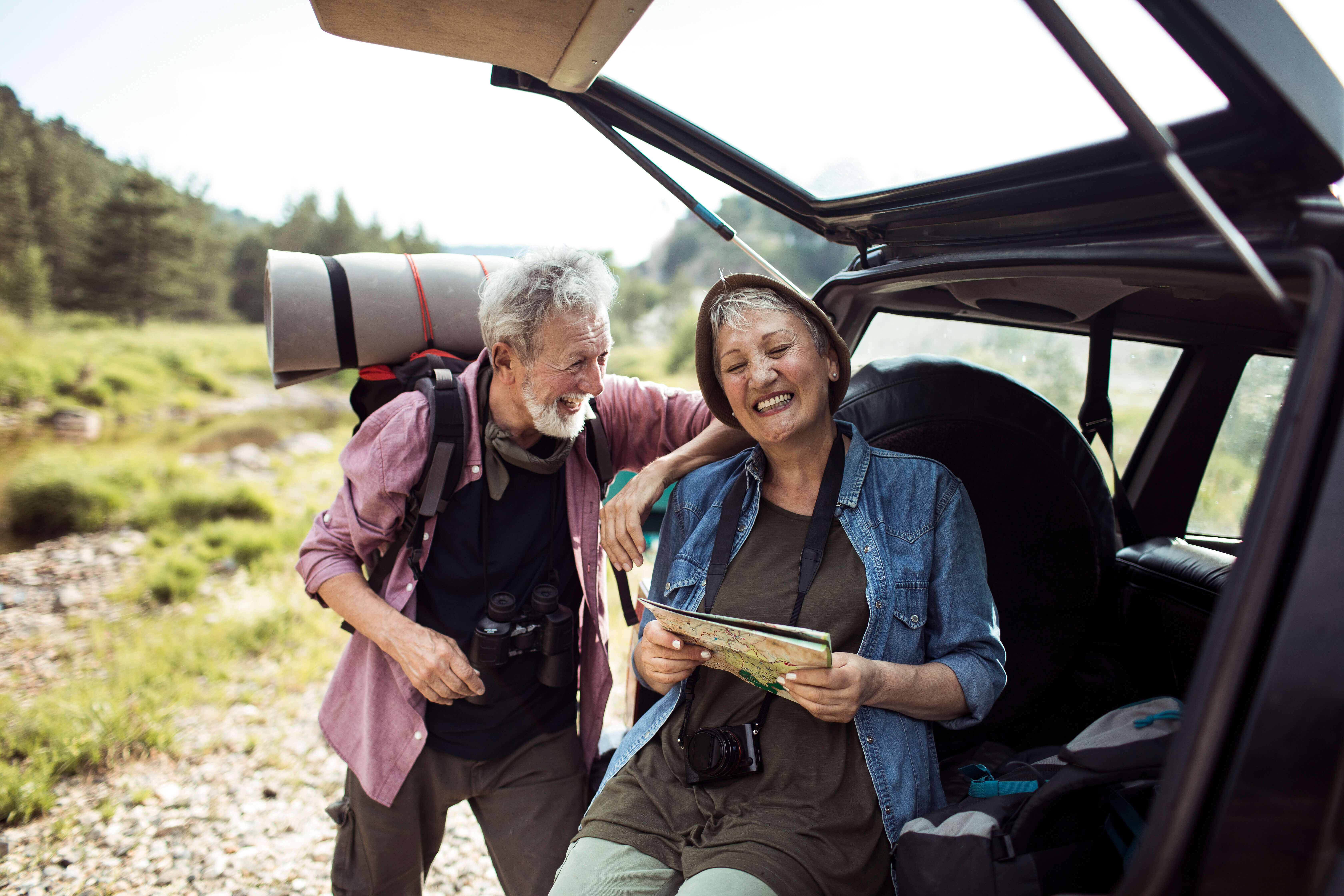 Older couple smiling and looking at map beside their car