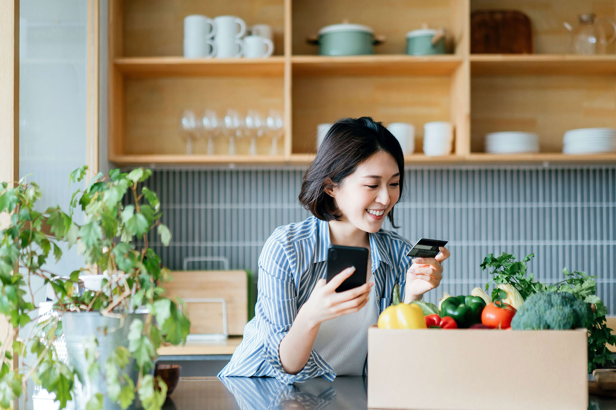 Woman smiling in kitchen with credit card and phone